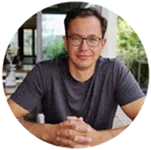 Mann mit Brille sitzt an einem Tisch in einem modernen Innenraum.